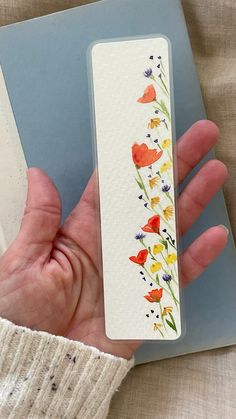 a hand holding a bookmark with flowers painted on it