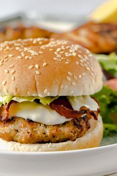 a chicken burger with lettuce, bacon and cheese on a plate next to some fries