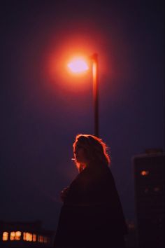 a woman standing under a street light at night with the sun shining on her face