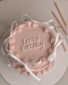 a pink birthday cake with the words happy birthday written in frosting and ribbons on it