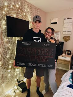 two people standing in a room holding a sign that says, there are strange things