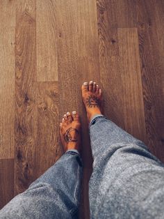 a person with tattoos on their feet standing on a wooden floor