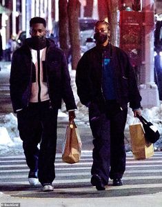 two men walking down the street with bags in their hands and one man wearing a face mask