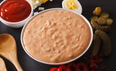 a bowl of dip surrounded by other foods and condiments on a black surface