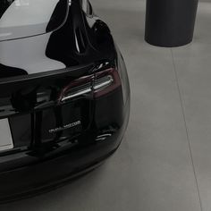 the back end of a black car parked in a garage next to two trash cans