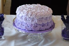 there is a cake on the table with purple frosting and flowers in glass vases