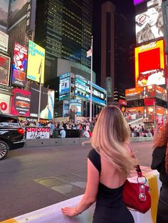 a woman in a black dress is sitting on a ledge looking at the city lights