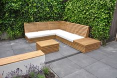 a wooden bench sitting on top of a cement floor next to a lush green wall