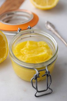 a glass jar filled with lemon curd next to sliced lemons and a spoon