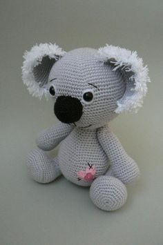 a crocheted koala bear sitting on top of a white table next to a pink flower