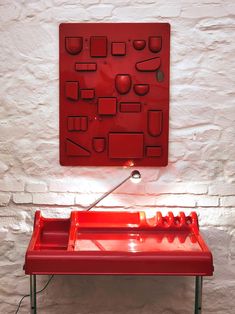 a red table with an object on it in front of a white brick wall and floor