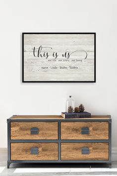 this is us wall art above a dresser in a room with white walls and wooden drawers