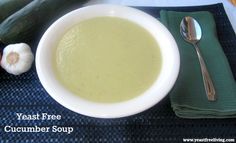 a white bowl filled with cucumber soup next to a green napkin and two silver spoons