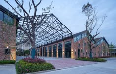 the building has many windows and is surrounded by plants, trees, and flowers in front of it