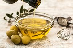 olives and oil being poured into a glass bowl