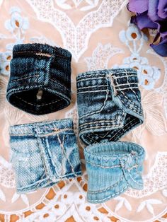 three pairs of jeans sitting on top of a lace doily next to purple flowers