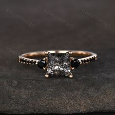 an engagement ring with black diamonds and a princess cut diamond in the center, on top of a rock