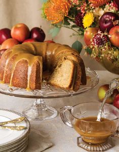 a bundt cake sitting on top of a glass plate next to a bowl of apples