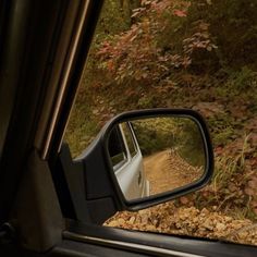 a car is seen in the rear view mirror as it drives down a dirt road