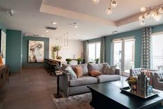 a living room filled with lots of furniture next to large window covered in light blue curtains