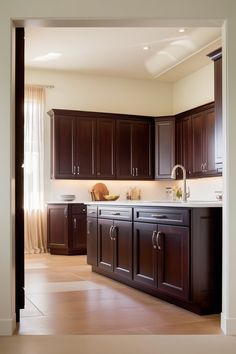 a large kitchen with dark wood cabinets and white counter tops is seen through an open doorway