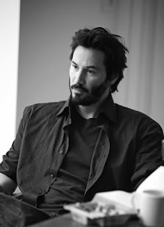 a man with a beard sitting at a table in front of a book and cup