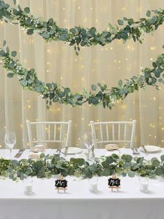 the table is decorated with greenery and place settings for dinner guests to sit at