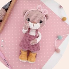 a crocheted teddy bear is sitting on a pink surface next to knitting supplies