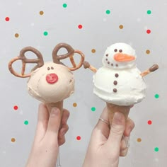 two people holding ice cream cones with reindeer noses and nose rings on them, one is frosting the other has pretzels