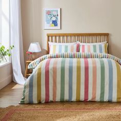 a bed with colorful striped sheets and pillows in a room next to a painting on the wall