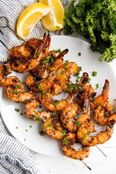 grilled shrimp on a white plate with lemon wedges and parsley next to it