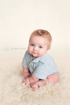 a baby is sitting on a fluffy white blanket and smiling at the camera while wearing a blue shirt