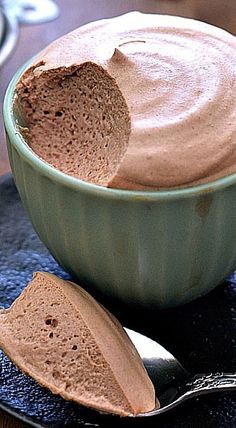 a bowl filled with chocolate frosting next to a spoon on a black tablecloth