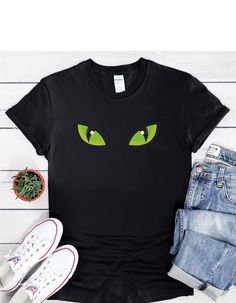 "Dive into the abyss of Halloween with our \"Monster Green Eyes\" T-shirt. This shirt features a pair of eerie green eyes that peer out from the darkness, capturing the mysterious allure of the season. Whether you're attending a Halloween party or just want to embrace the enigmatic, this shirt adds a touch of intrigue to your attire. Gaze into the unknown and let Halloween's mysteries unfold! This unisex soft-style t-shirt puts a new spin on casual comfort. Made from very soft material which is 100% cotton. The shoulders have twill tape for improved durability. There are no side seams. The collar is made with ribbed knitting to prevent curling damage.  .: 100% ring-spun cotton (fiber content may vary for different colors) .: Light fabric (4.5 oz/yd² (153 g/m .: Eurofit .: Tear-away label . Green Glow In The Dark Crew Neck T-shirt, Green Halloween T-shirt For Streetwear, Green Halloween T-shirt With Character Print, Eyes Halloween, Halloween Mystery, Into The Abyss, Halloween Graphic, Into The Unknown, Family Halloween