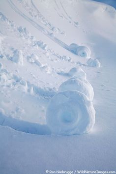 a snowman made out of snow on the side of a snowy hill with trees in the background