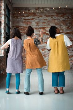 three women standing next to each other in front of a brick wall with lights on it