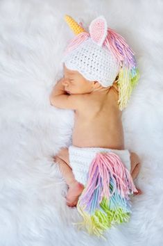 a baby wearing a crochet unicorn hat and diaper is sleeping on a fluffy white blanket