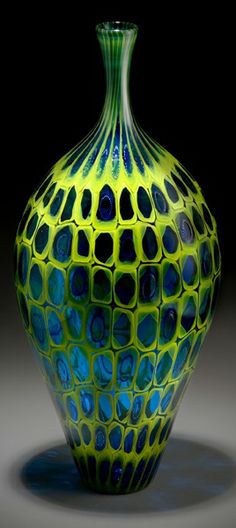 a green and blue glass vase sitting on top of a table next to a black background