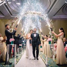 the bride and groom are walking down the aisle with sparklers in the air above them