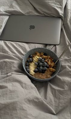 a bowl of oatmeal with blueberries and bananas in front of an apple laptop