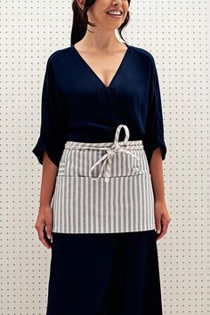 a woman standing in front of a white wall wearing a black and grey striped apron