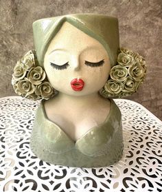 a ceramic sculpture of a woman with her eyes closed on a white doily covered table