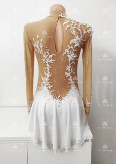 the back of a white and gold figure skating dress with flowers on it's chest