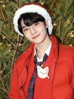 a young man wearing a santa hat next to a christmas tree