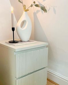 a white vase sitting on top of a dresser next to a candle