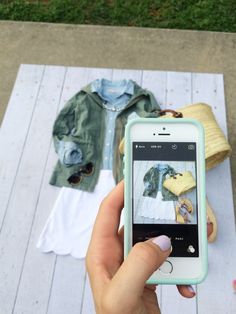 a person holding an iphone taking a photo of clothes on a wooden table with grass in the background