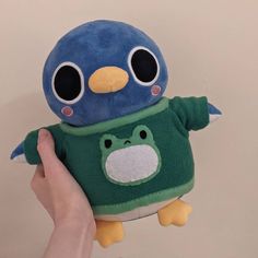 a person holding up a stuffed animal with big eyes and a green t - shirt