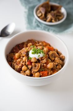 a white bowl filled with food next to two spoons on top of a table