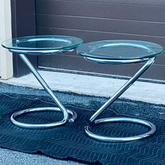 two glass tables sitting next to each other on the ground in front of a door