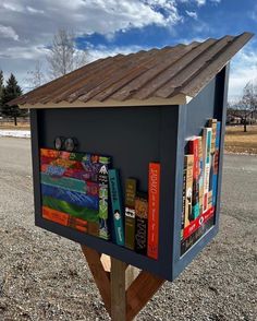 a mailbox with books on it sitting in the middle of a gravel road next to a field